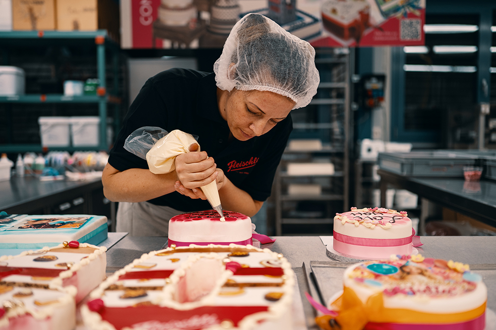 Eine Konditorin von Fleischli dekoriert verschiedene Torten in der Produktionsstätte in Niederglatt.